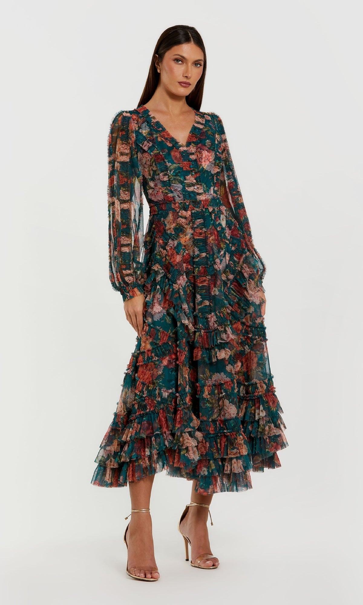 A woman stands against a white background wearing the Mac Duggal 8348 Floral Wedding Guest Dress, featuring long sleeves, a V-neck, ruffled tiered A-line skirt, and gold high-heeled sandals.